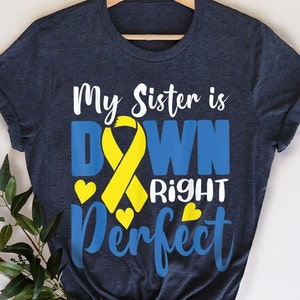 May include: A navy blue t-shirt with the text "My Sister is Down Right Perfect" in white and blue lettering. A yellow ribbon is in the centre of the text. The ribbon is a symbol of Down Syndrome awareness.