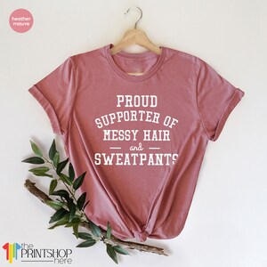 May include: A heather mauve t-shirt with the text "PROUD SUPPORTER OF MESSY HAIR and SWEATPANTS?" printed in white.