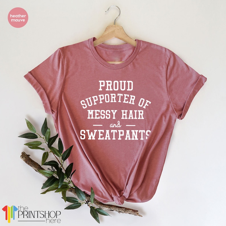 May include: A heather mauve t-shirt with the text "PROUD SUPPORTER OF MESSY HAIR and SWEATPANTS?" printed in white.