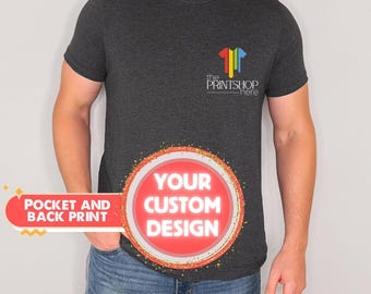 May include: A dark gray t-shirt with a pocket on the left side. The t-shirt has a logo on the pocket that says "the PRINTSHOP here". The t-shirt also has a red circle with the text "YOUR CUSTOM DESIGN" on the front.