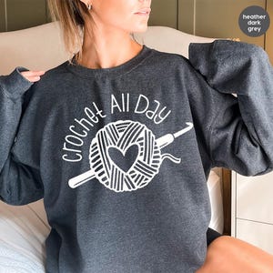 May include: A heather dark grey sweatshirt with the text "crochet all day" in white. The design features a ball of yarn with a heart and a crochet hook.