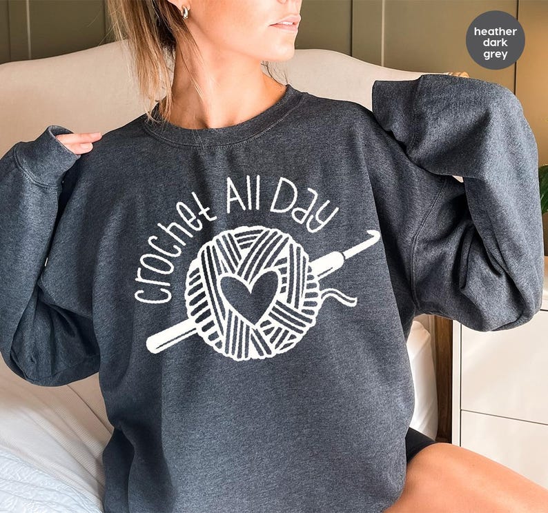 May include: A heather dark grey sweatshirt with the text "crochet all day" in white. The design features a ball of yarn with a heart and a crochet hook.