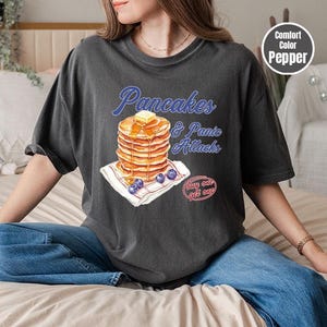 a woman sitting on a bed with a stack of pancakes on her shirt