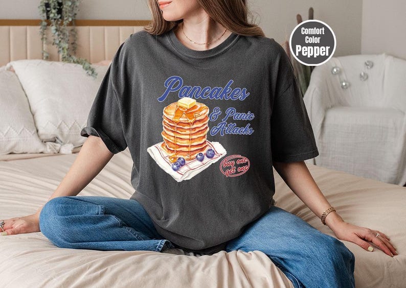 a woman sitting on a bed with a stack of pancakes on her shirt