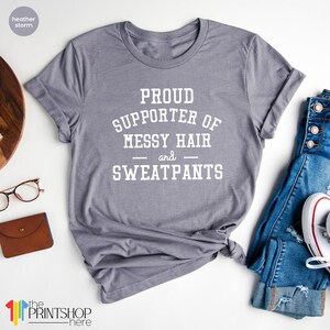 May include: Gray t-shirt with white text that reads "Proud Supporter of Messy Hair and Sweatpants".