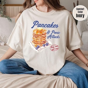 a woman sitting on a bed with a stack of pancakes on her shirt
