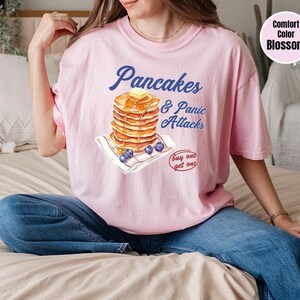 a woman sitting on a bed wearing a pink shirt