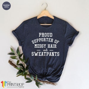 May include: A heather navy blue t-shirt with white text that reads "Proud Supporter of Messy Hair and Sweatpants".