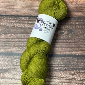 May include: A skein of green yarn with a white label wrapped around it. The label features a mermaid illustration and the text "Happy Mermaid Yarn Co. Hand dyed". The yarn is a vibrant shade of green.