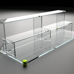 May include: A clear acrylic shelf unit with three tiers. The shelf unit has a rectangular base and is supported by four green plastic feet.