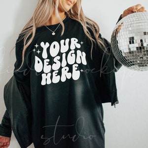 May include: Black long-sleeve shirt with the text "YOUR DESIGN HERE" in white, with star accents. A silver disco ball is held in the right hand. The shirt is paired with a black jacket.