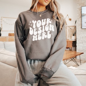 May include: A gray sweatshirt with the text "YOUR DESIGN HERE" in white, retro-style lettering. The sweatshirt has long sleeves and a crew neck.
