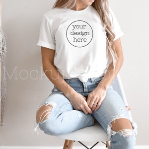 Pode incluir: Uma camiseta branca com um c&iacute;rculo na frente que diz "your design here". A camiseta est&aacute; sendo usada por uma pessoa sentada em uma cadeira branca. A pessoa est&aacute; usando jeans azul.