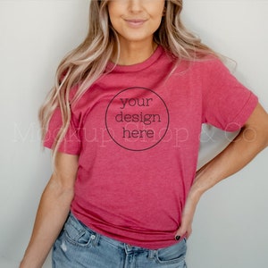 Puede incluir: Una camiseta roja con el texto "your design here" en un círculo negro. La camiseta es de cuello redondo y se lleva con vaqueros azules. La modelo tiene el pelo largo y rubio.