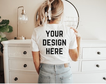 May include: A white t-shirt with the text "YOUR DESIGN HERE" printed on the back. The shirt is being worn by a person with blonde hair and blue jeans.
