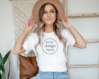 May include: A woman wearing a white t-shirt with the text "your design here" in a circle. She is wearing a brown hat and blue jeans.