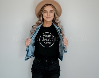 以下が含まれることがあります： 白い円の中に「your design here」という文字が書かれた黒いTシャツを着て、デニムジャケットと茶色の帽子をかぶった女性。