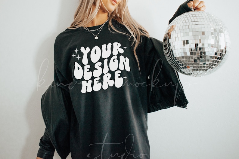 May include: A black sweatshirt with the text "YOUR DESIGN HERE" in white, with a retro font style. The model is wearing the sweatshirt and holding a silver disco ball.