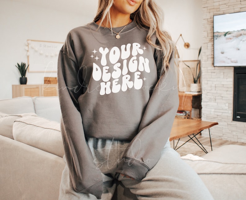 May include: A gray sweatshirt with the text "YOUR DESIGN HERE" in white, retro-style lettering. The sweatshirt has long sleeves and a crew neck.