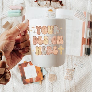 May include: White ceramic mug with a design that says "YOUR DESIGN HERE" in colorful, retro-style letters. The mug has a gold cross and glitter accents.