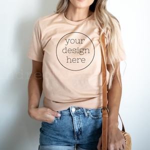 Könnte beinhalten: Ein helles, pfirsichfarbenes T-Shirt mit einem schwarzen Kreis auf der Vorderseite, auf dem "your design here" steht.