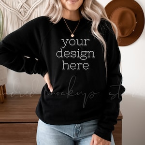 以下が含まれることがあります： クルーネックと長袖の黒いスウェットシャツ。スウェットシャツの前には「your design here」というテキストがプリントされています。