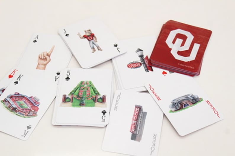 Puede incluir: Una baraja de cartas con varias ilustraciones. Las cartas presentan im&aacute;genes de un estadio, un gesto con la mano, una mascota y el texto "BOOMER". Los dorsos de las cartas son rojos con un logotipo blanco.