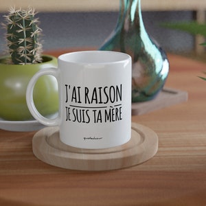 Puede incluir: Taza de cer&aacute;mica blanca con texto negro que dice "J'AI RAISON JE SUIS TA M&Egrave;RE". La taza est&aacute; sobre un posavasos de madera.