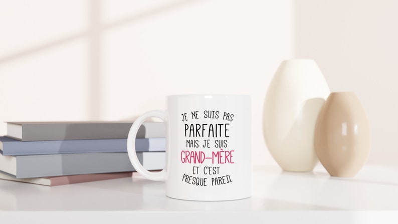 May include: White ceramic mug with a black and pink design. The text on the mug reads "Je ne suis pas parfaite mais je suis grand-m&egrave;re et c'est presque pareil".