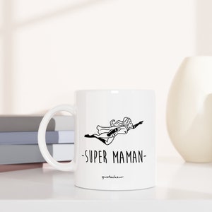 May include: White ceramic mug with a black line drawing of a woman flying with the text "SUPER MAMAN" on the front.