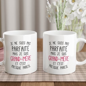 May include: Two white ceramic mugs with black text that reads "Je ne suis pas parfaite mais je suis grand-m&egrave;re et c'est presque pareil". The text "grand-m&egrave;re" is in pink.