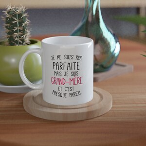 May include: White ceramic mug with black text that reads "Je ne suis pas parfaite mais je suis grand-m&egrave;re et c'est presque pareil". The text "grand-m&egrave;re" is in pink.