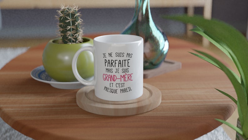 May include: White ceramic mug with black text that reads "Je ne suis pas parfaite mais je suis grand-m&egrave;re et c'est presque pareil". The text "grand-m&egrave;re" is in pink.