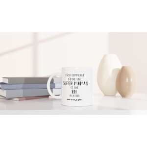 May include: White ceramic mug with black text that reads "C'EST COMPLIQUE D'&Ecirc;TRE UNE SUPER MAMAN ET UNE RH A LA FOIS mais ca va je g&egrave;re..."
