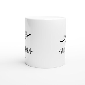 May include: White ceramic mug with a black silhouette of a person flying with the text "Superman" on the left side and "Superwoman" on the right side.