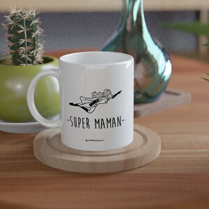 May include: White ceramic mug with a black illustration of a woman flying with the text "SUPER MAMAN" on the front.