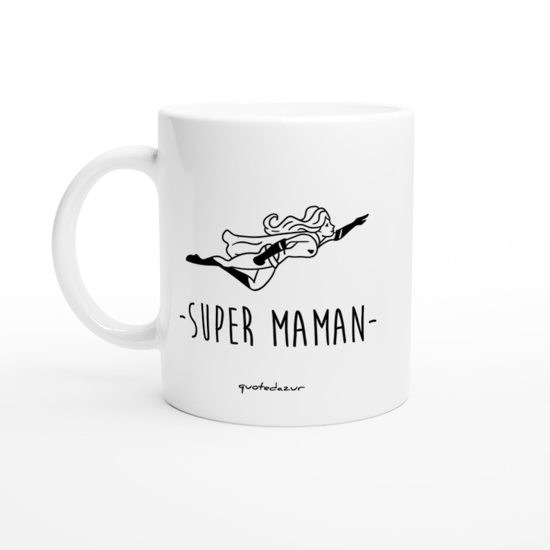 May include: White ceramic mug with a black line drawing of a woman flying with a cape and the text "SUPER MAMAN" and the text "quotedezur" at the bottom.