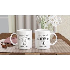 May include: Two white ceramic mugs with black text that reads "C'EST COMPLIQUE D'&Ecirc;TRE UNE SUPER MAMAN ET UNE RH A LA FOIS mais ca va je g&egrave;re."
