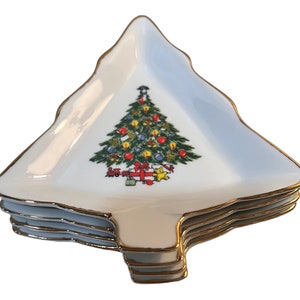May include: Set of four white ceramic Christmas tree-shaped serving dishes with gold trim. Each dish features a colorful illustration of a Christmas tree with ornaments and presents.