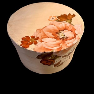 May include: A round, cream-colored box with a floral design. The flowers are painted in shades of orange, pink, and green.