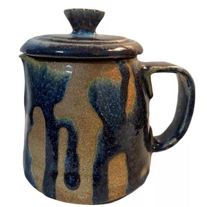 May include: A brown and blue ceramic teapot with a lid. The teapot has a unique drip glaze design.