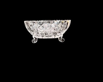 May include: A clear glass bowl with a cut glass design and three legs. The bowl is oval shaped and has a shiny finish.
