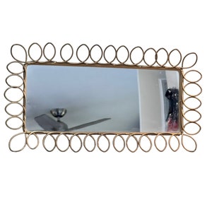 May include: A gold-toned rectangular mirror with a decorative frame made of interlocking circles.