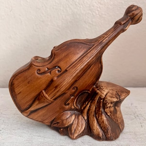 May include: A brown ceramic vase shaped like a violin with a carved wooden base. The vase is a decorative piece for displaying flowers or other small plants.