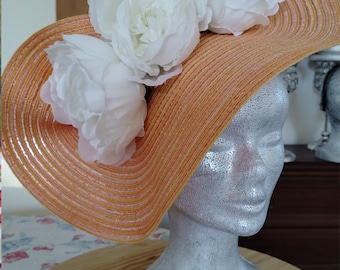 Orange ceremonial wide-brimmed hat adorned with ecru roses and a large bow