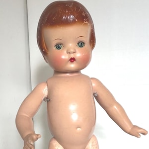 May include: Vintage doll with a painted face, red hair, and blue eyes. The doll has a classic design with articulated arms and legs. The doll is standing on a metal stand. A collectible item.