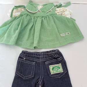 Puede incluir: Un top de muñeca de cuadros vichy verdes y blancos con cuello redondo y mangas cortas abullonadas, junto con pantalones cortos de mezclilla azul oscuro con cintura elástica y un parche de Cabbage Patch Kids en el bolsillo trasero y etiqueta.