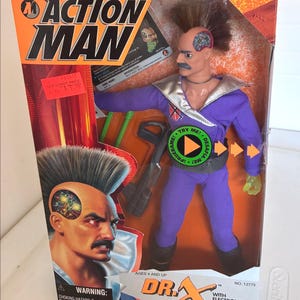 May include: Action Man Dr. X action figure in original packaging. The figure is wearing a purple jumpsuit with a silver collar and has a mohawk hairstyle. The packaging features the Action Man logo and the text "WITH ELECTRONIC BRAIN AND LASER EYE."