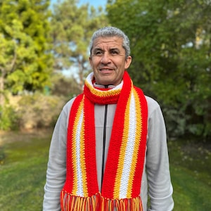 Puede incluir: Bufanda de crochet hecha a mano con rayas rojas, amarillas y blancas y flecos a juego. La bufanda se lleva alrededor del cuello. Un accesorio vibrante y un accesorio de invierno acogedor.