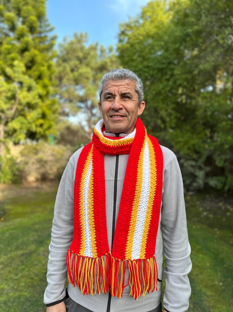 Puede incluir: Bufanda de crochet hecha a mano con rayas rojas, amarillas y blancas y flecos a juego. La bufanda se lleva alrededor del cuello. Un accesorio vibrante y un accesorio de invierno acogedor.